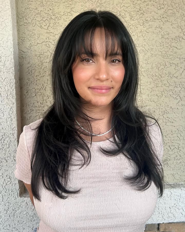 Medium length layered dark hair with wispy bangs and natural volume.