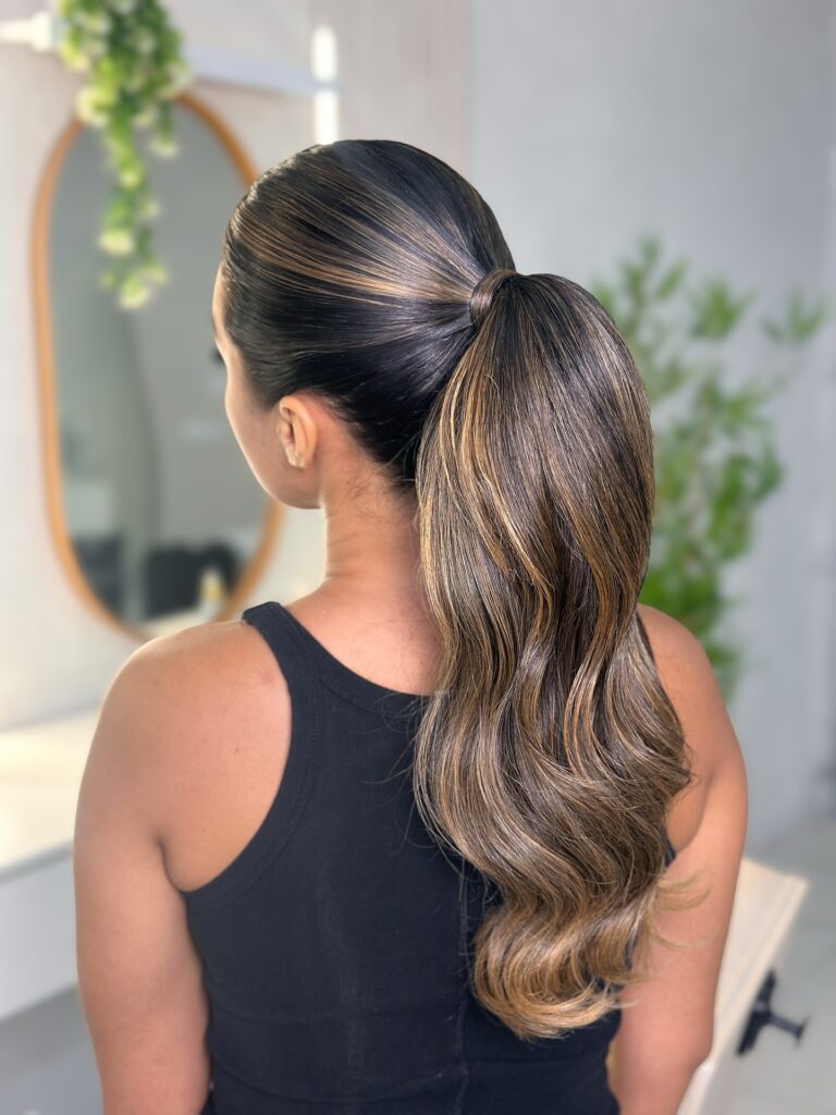 Low ponytail with a sleek crown and softly waved brunette ends.