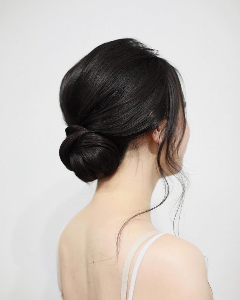 A woman from the back showing a elegant low chignon bun in dark hair with soft face framing strands.