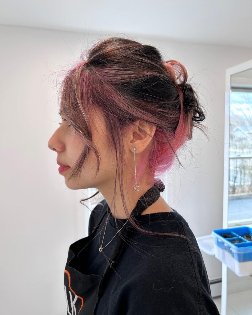 A side profile photograph of a young woman featuring a vibrant two-tone black and pink hairstyle styled into a textured and voluminous updo.