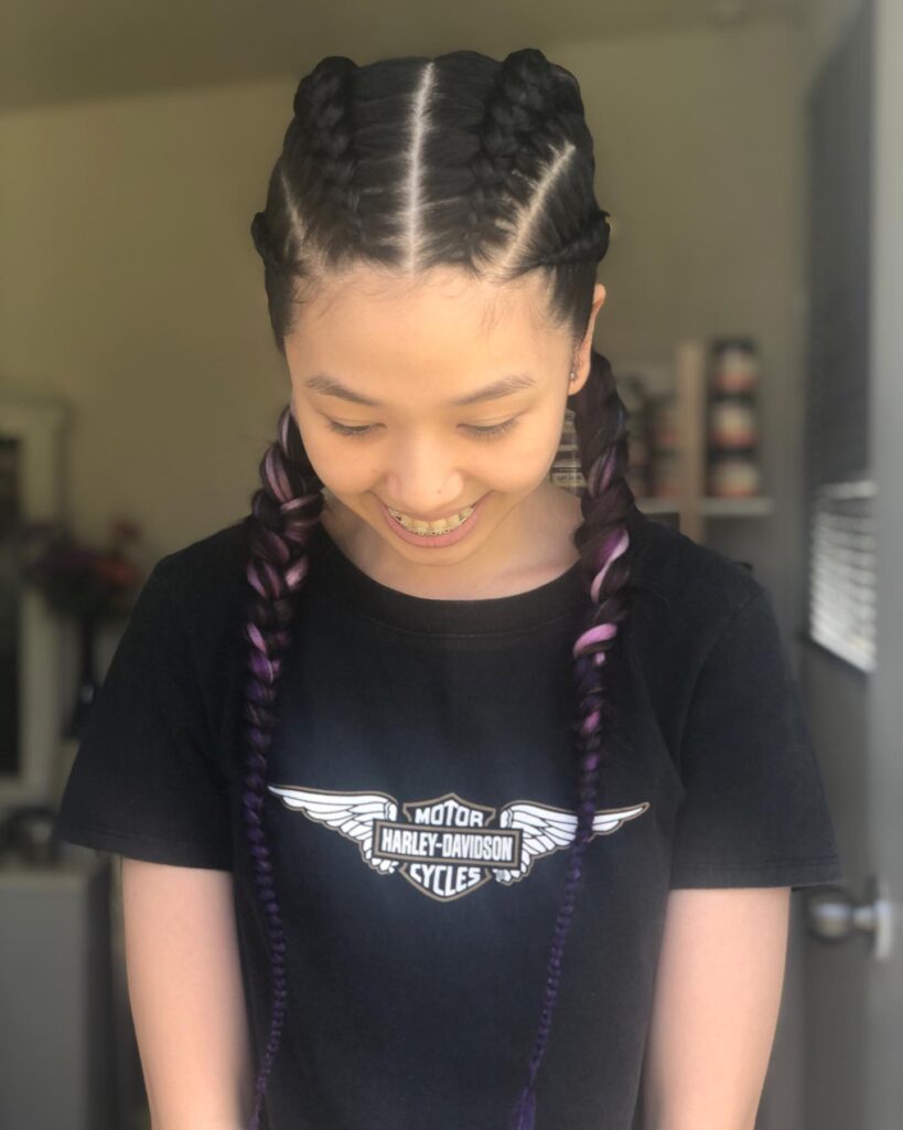 A girl smiling and looking down while wearing black and purple ombre Dutch braids that fall over her shoulders.