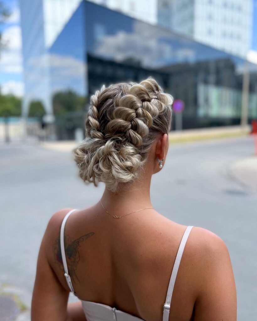 A woman from the back showing voluminous ash-blonde Dutch braids gathered into a textured low bun.