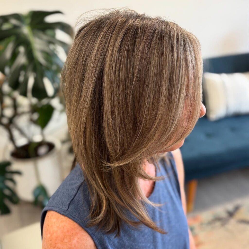 A woman from the side is showing a medium-length hairstyle with layered caramel brown hair and soft face-framing pieces.