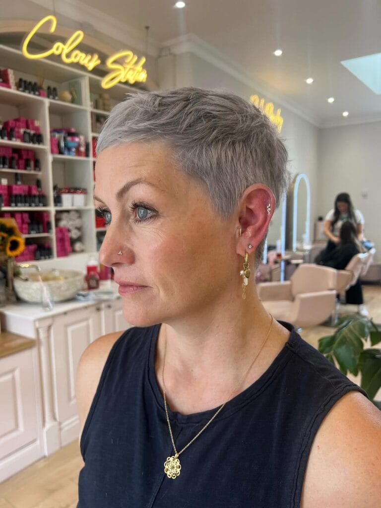 A woman with a very short textured pixie cut in a trendy lilac silver shade, showing off a clean side profile.