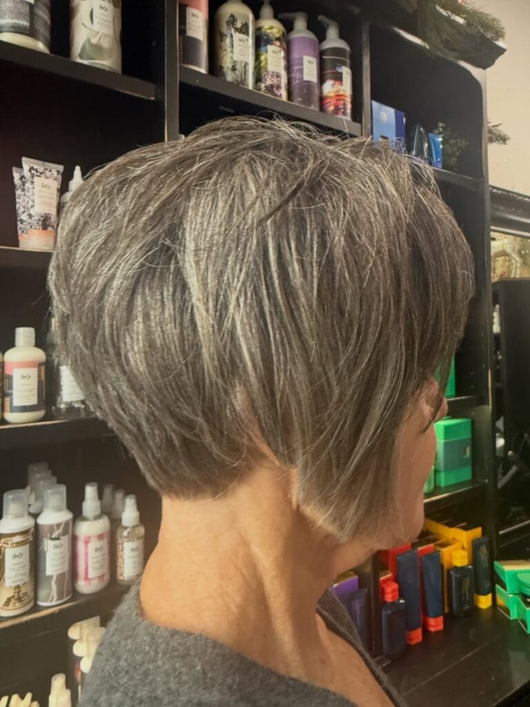 A woman from the side showing a short inverted bob with textured gray hair and an angled front.