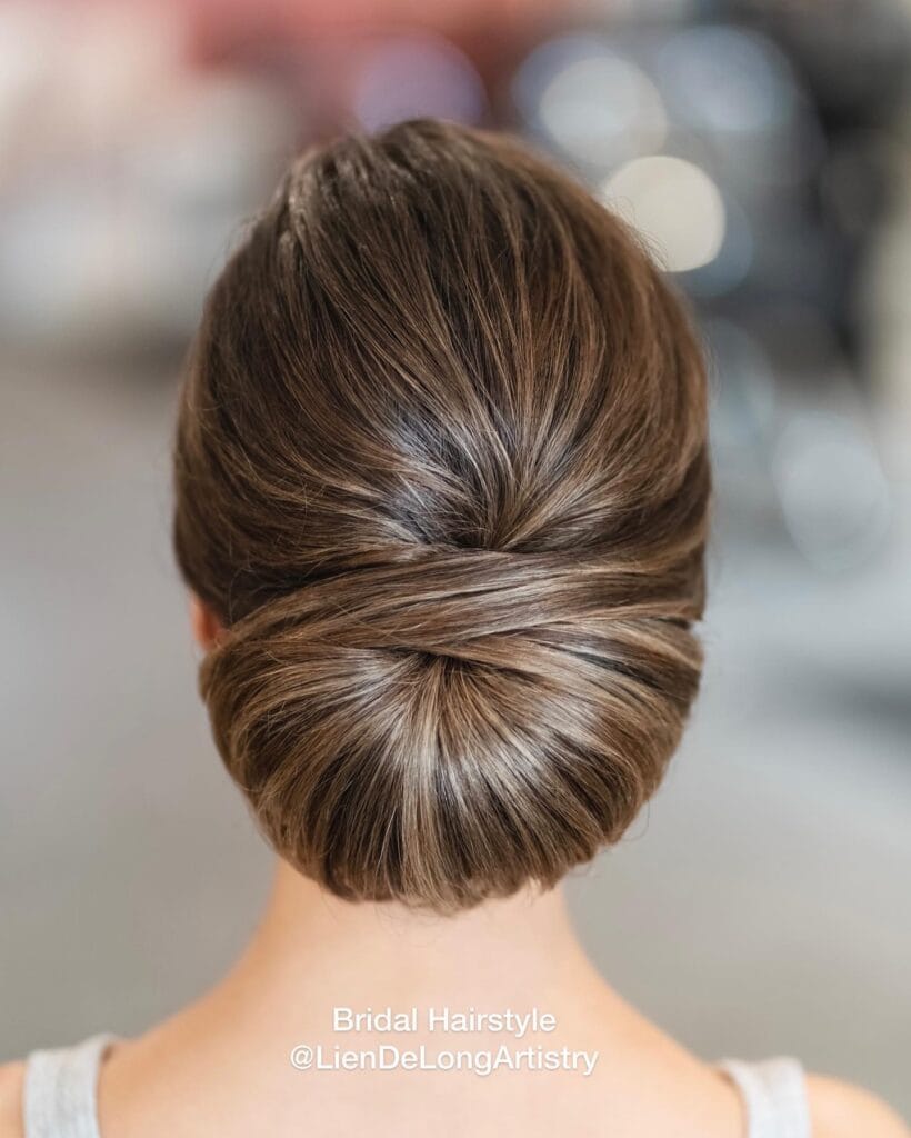 A back view of a woman with ash-brown highlighted hair styled in a smooth and elegant low chignon.