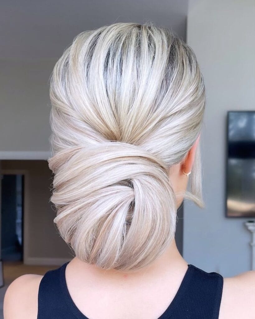 A back view of a woman with icy platinum blonde hair styled in a large and smooth wrapped low chignon.