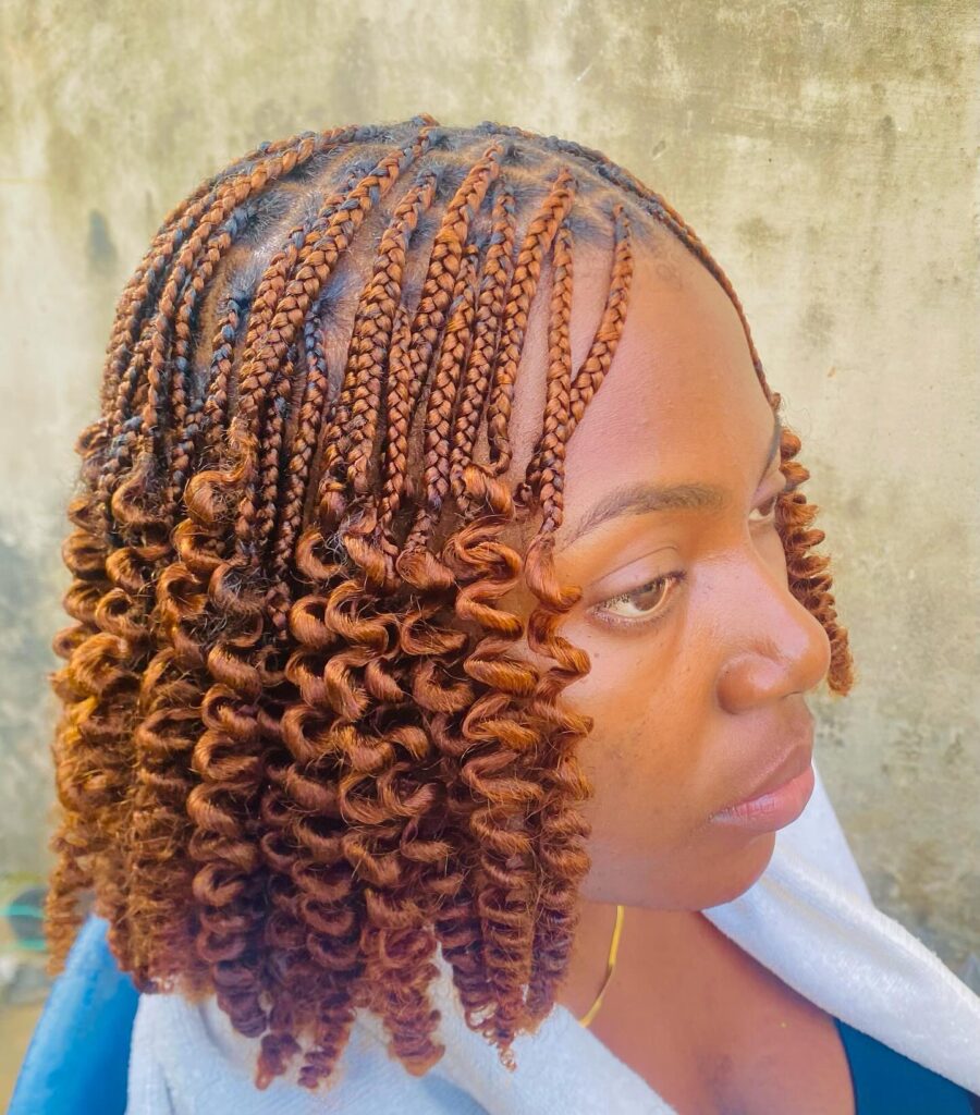 A woman with bright copper braids that end in tight spiral curls styled in a short bob.