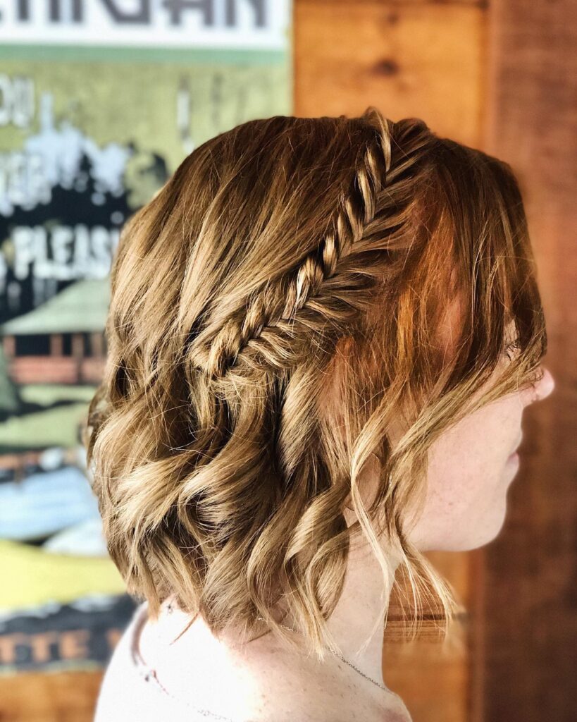 A side view of a woman with golden blonde wavy hair featuring a tight fishtail braid pinned to the side.