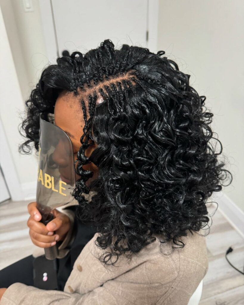 A woman with shiny black shoulder-length curls featuring a small section of microbraids along the side part.