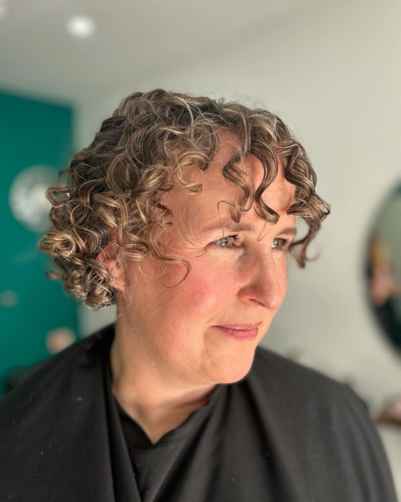 A woman with a short curly bob featuring defined ash brown ringlets and a curly fringe.