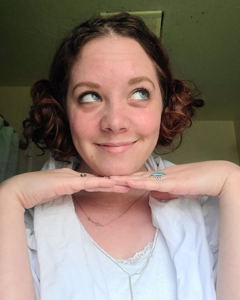 A woman with short auburn curls styled into two low space buns on either side of her head.