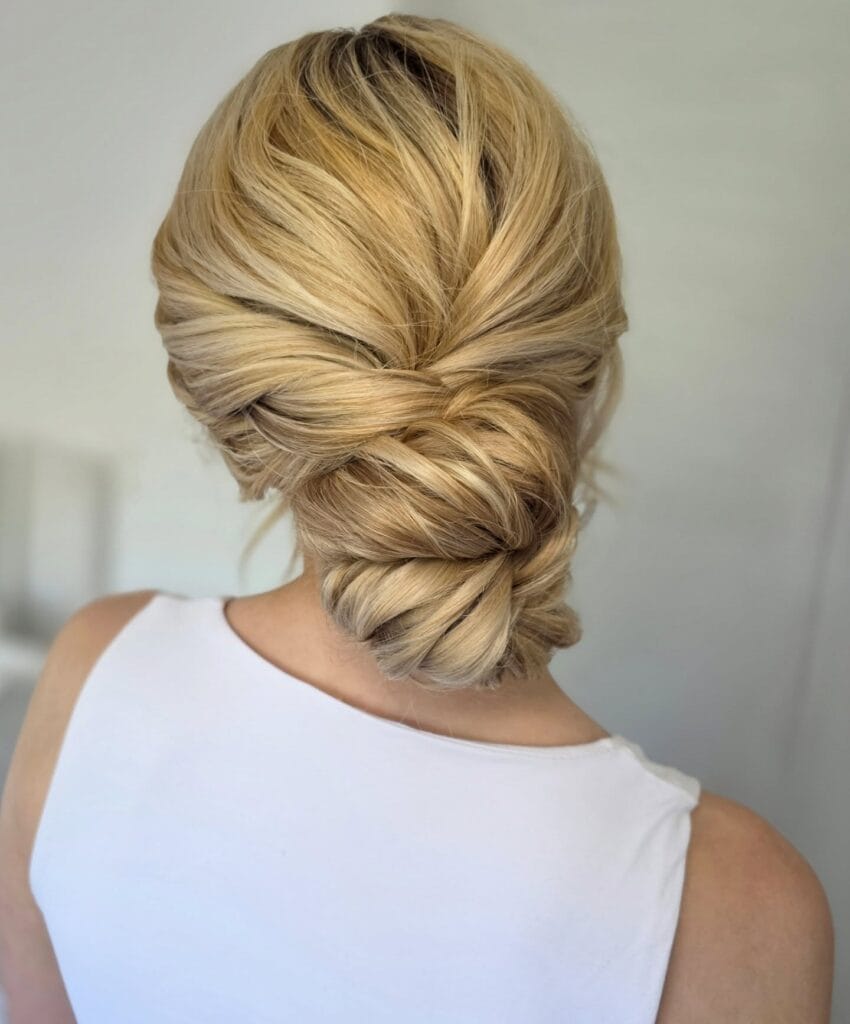 A back view of a woman with blonde hair styled into a soft and intricate braided low bun at the neck.