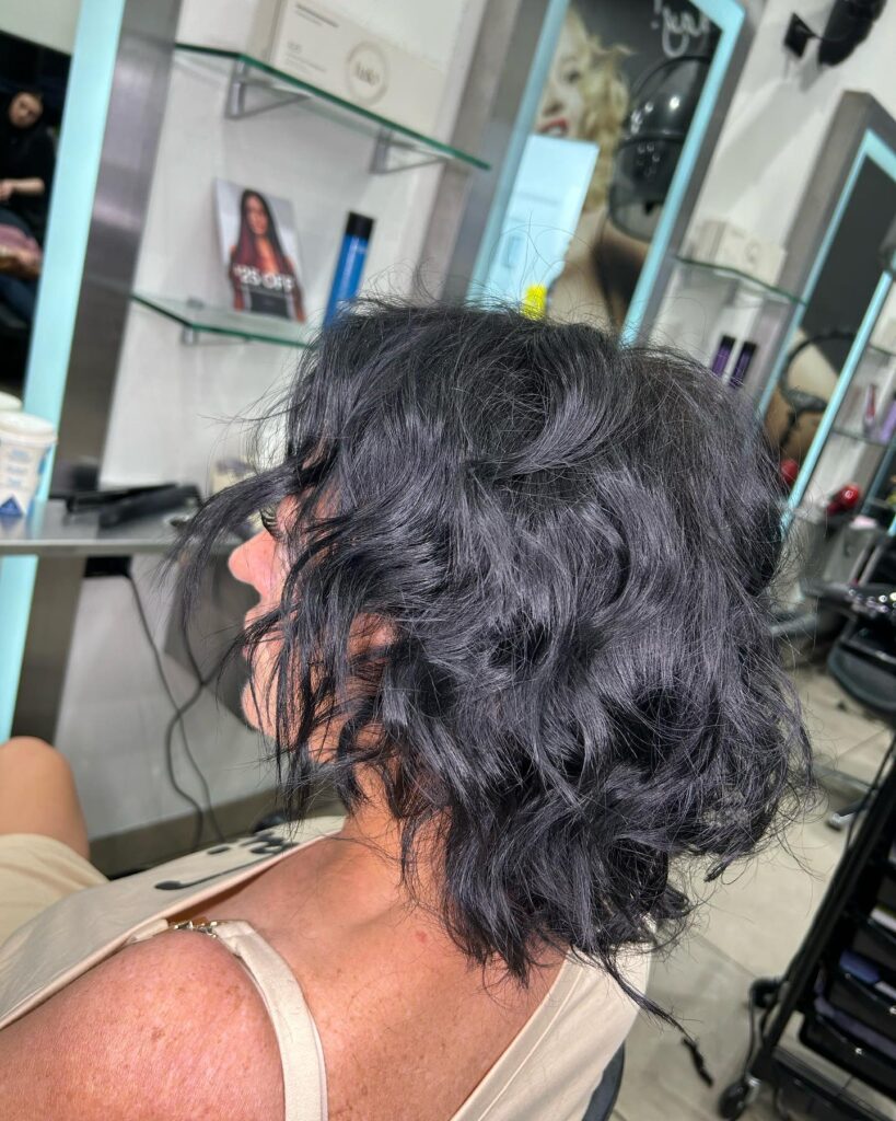 A side profile of a woman in a salon showing off a short, wavy bob in a deep black shade.