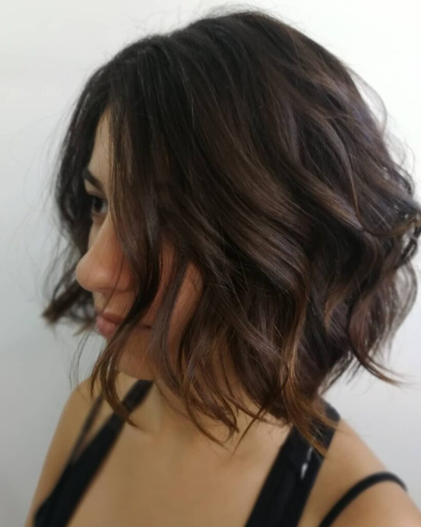 A side view of a woman with a tousled chin-length brunette bob styled in soft waves.