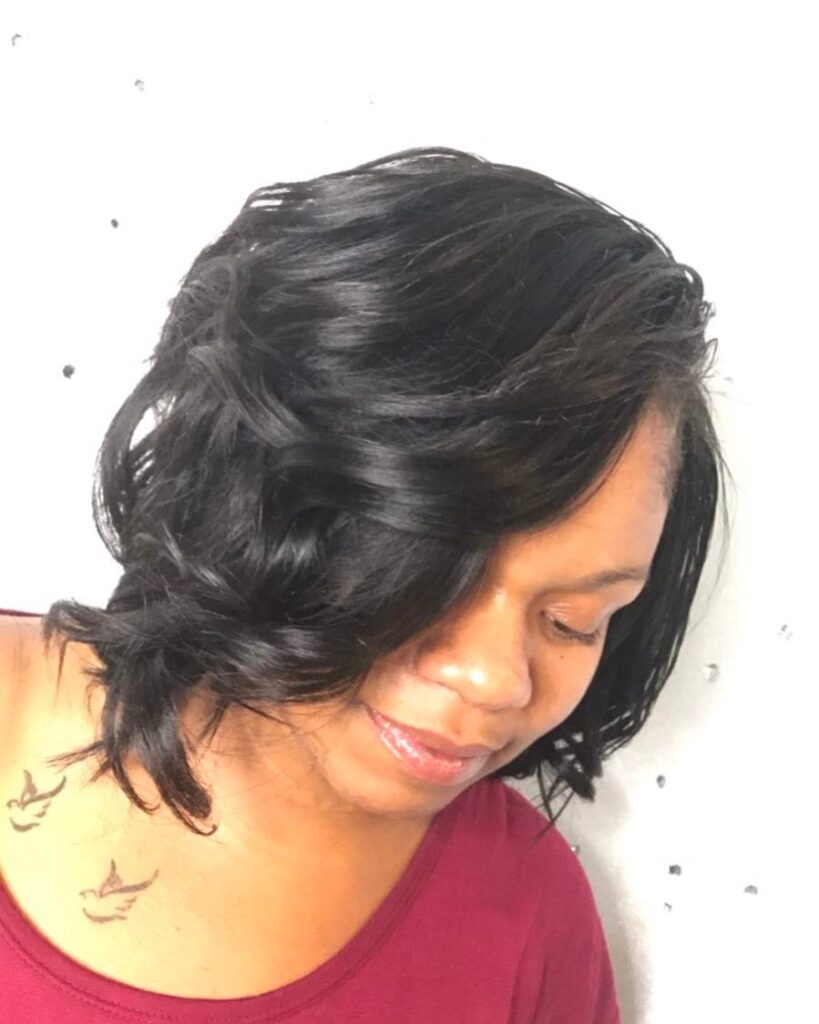 A woman with glossy short black curls styled in an asymmetrical side-swept look.