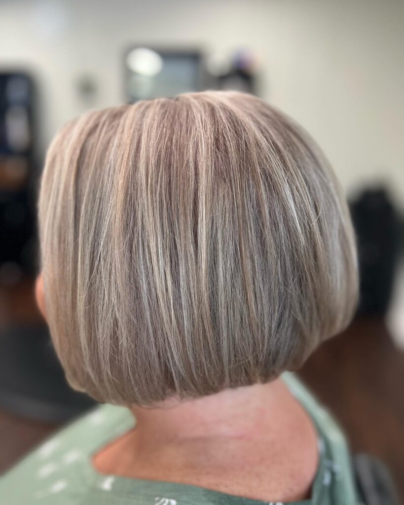 A back view of a woman with a silky ash blonde tapered short bob featuring smooth straight hair and a rounded silhouette.