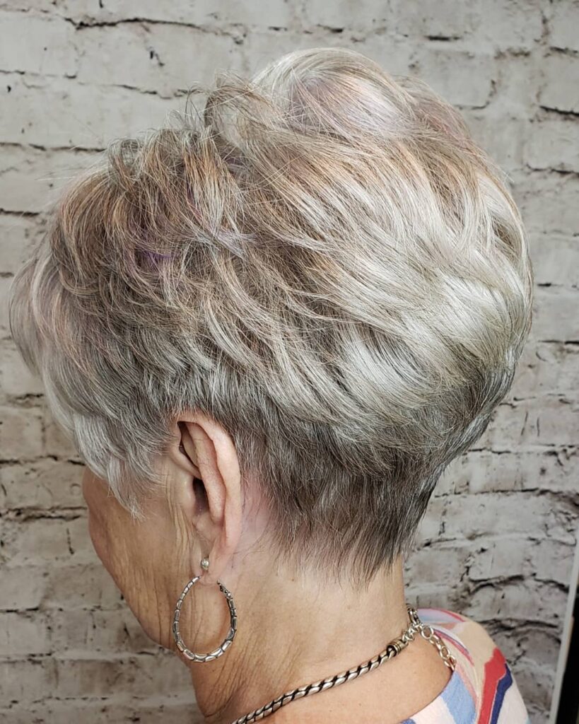 A backside view of a woman with a textured silver pixie cut featuring feathered layers and a neat tapered nape.