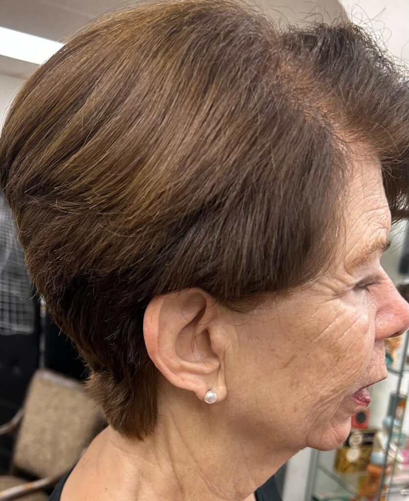 A side profile of a woman with a warm chestnut brown tapered haircut featuring soft layers swept back from the face.
