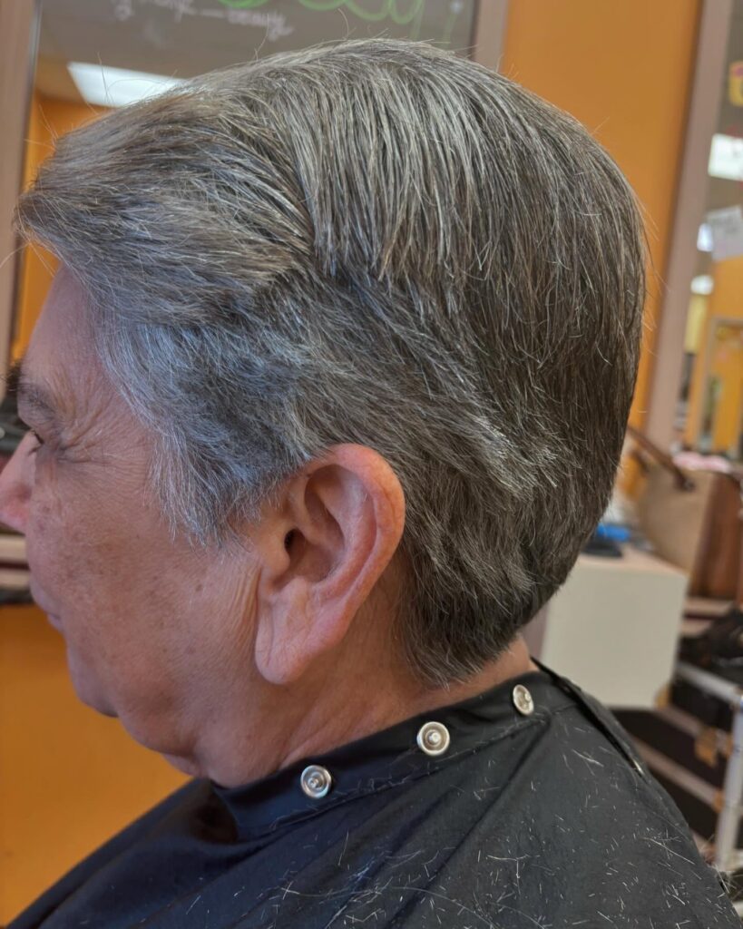 A side profile of a woman with a natural salt and pepper tapered short haircut featuring a clean nape and side-swept top.