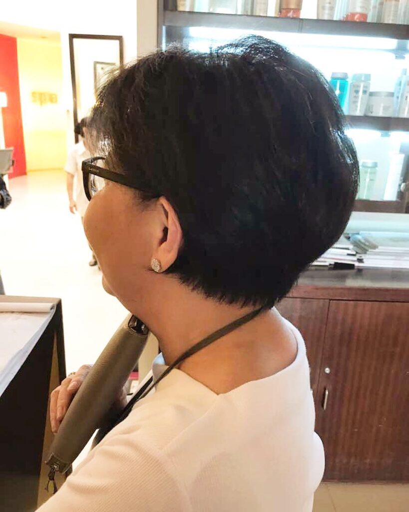 A sideback view of a woman with a sleek, jet black, stacked tapered haircut featuring a rounded silhouette and clean nape.