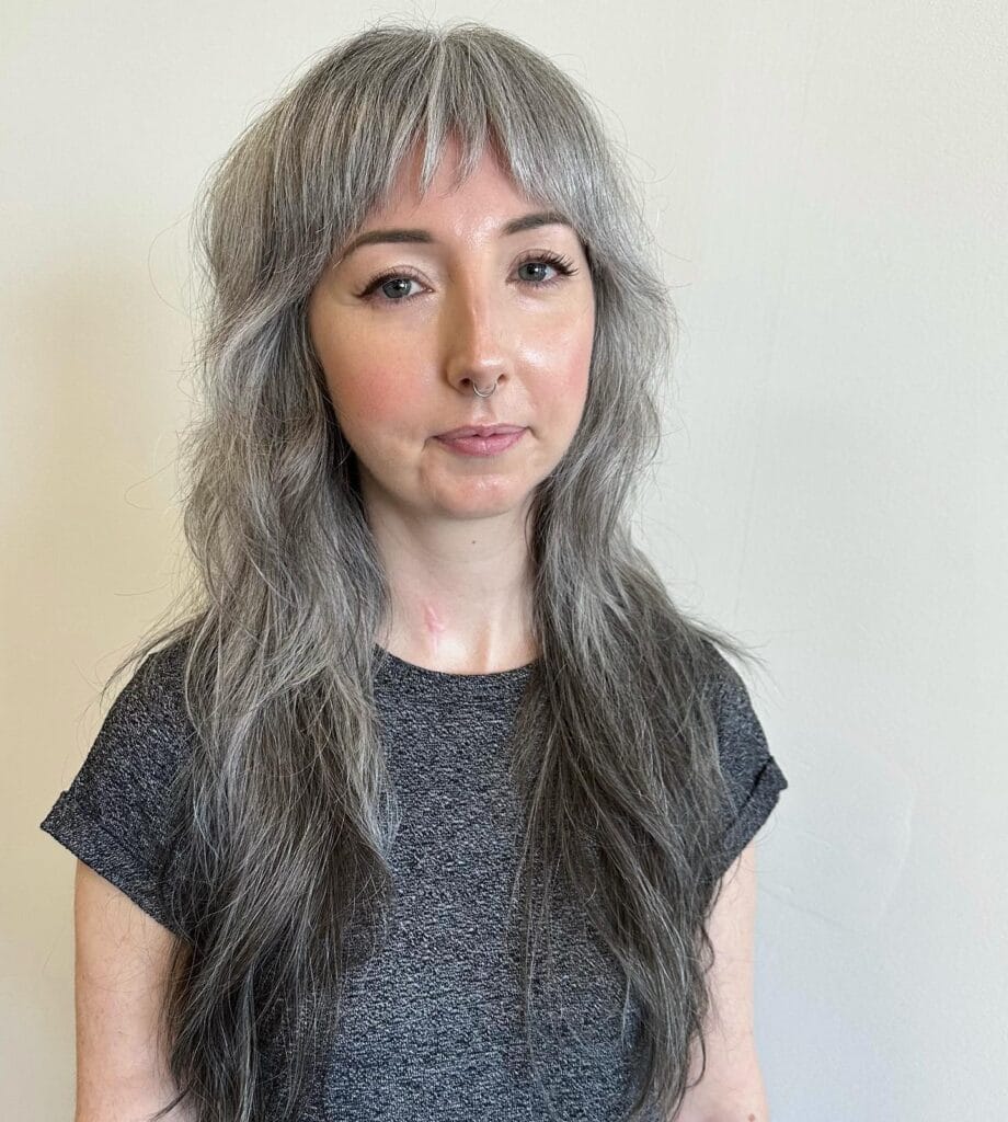 A woman with long, layered silver hair and soft, piecey bangs smiling slightly for a photo.