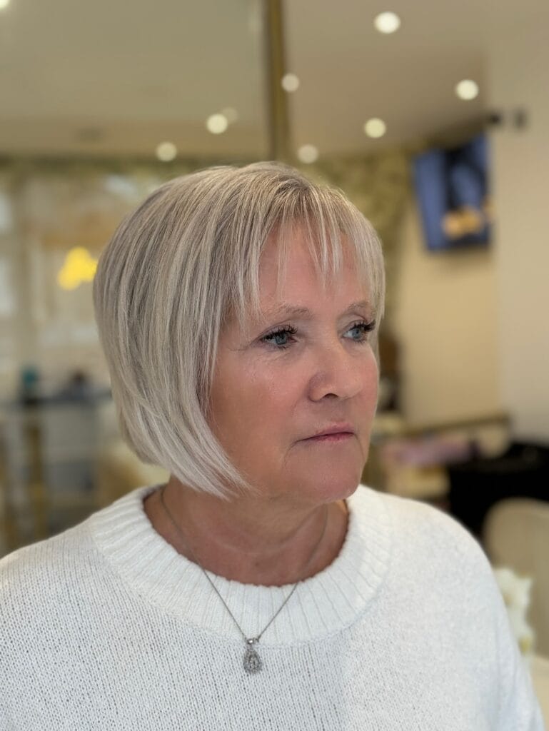 A woman with a sleek, platinum blonde, straight bob haircut and thin, wispy bangs is looking to the side.