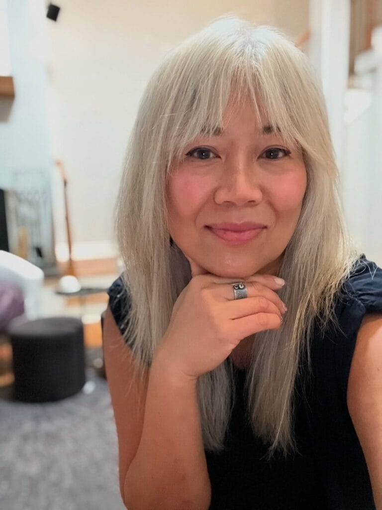 A smiling woman with long, straight, silver hair and feathered curtain bangs.