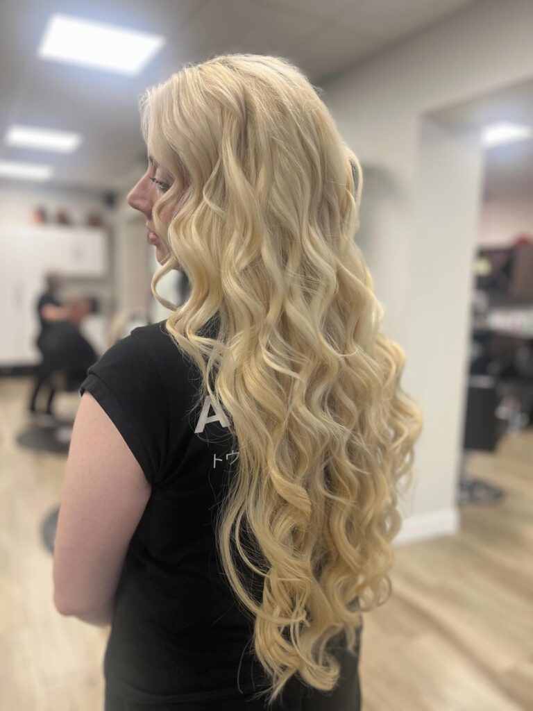 A woman with very long platinum blonde hair styled in deep mermaid waves posing in a salon.