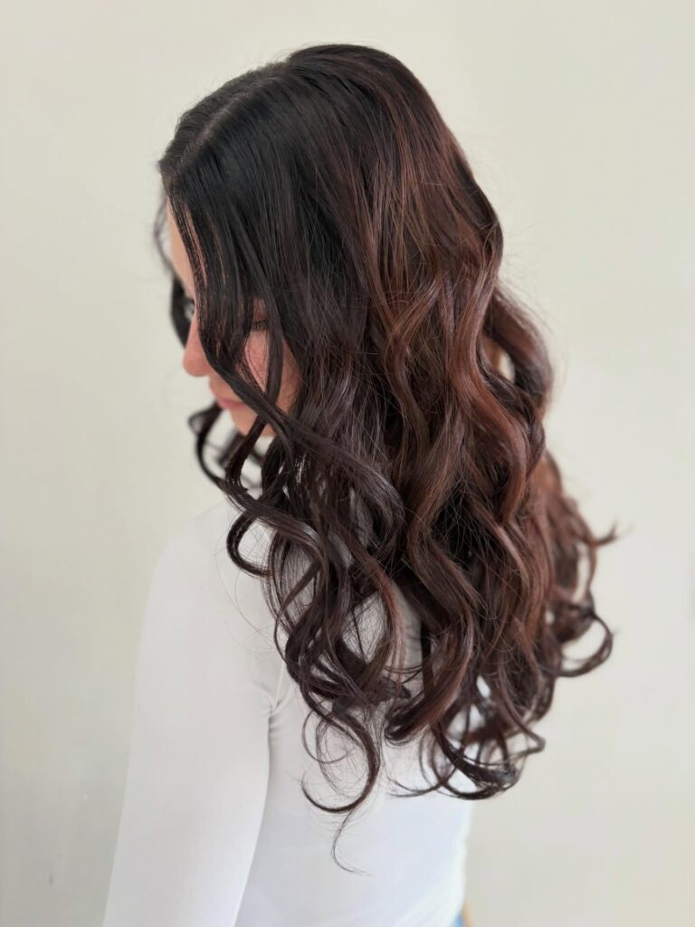 A woman with long mahogany brown hair styled into defined bouncy spiral curls.