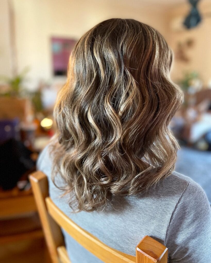 Shoulder-length brown wavy hair with soft layers and subtle blonde highlights adding dimension.