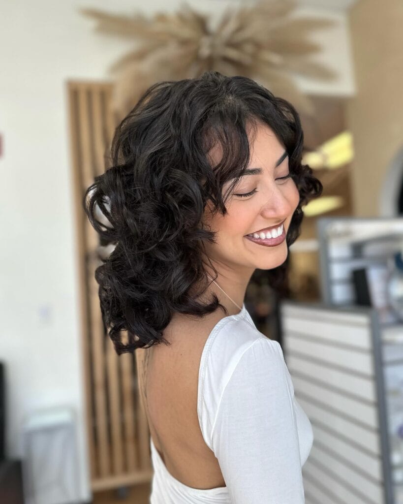 Short dark wavy hair with soft curls and playful layered texture.