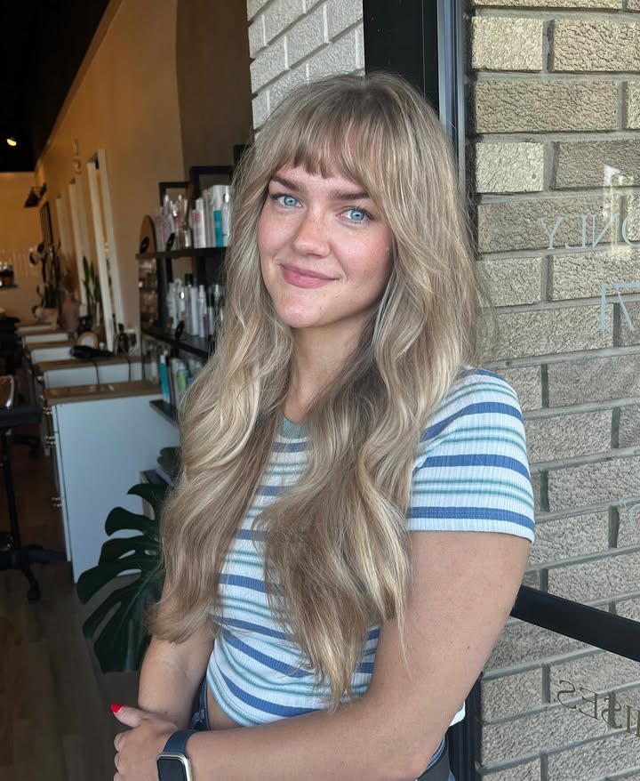 Long wavy blonde hair with full soft bangs across the forehead.