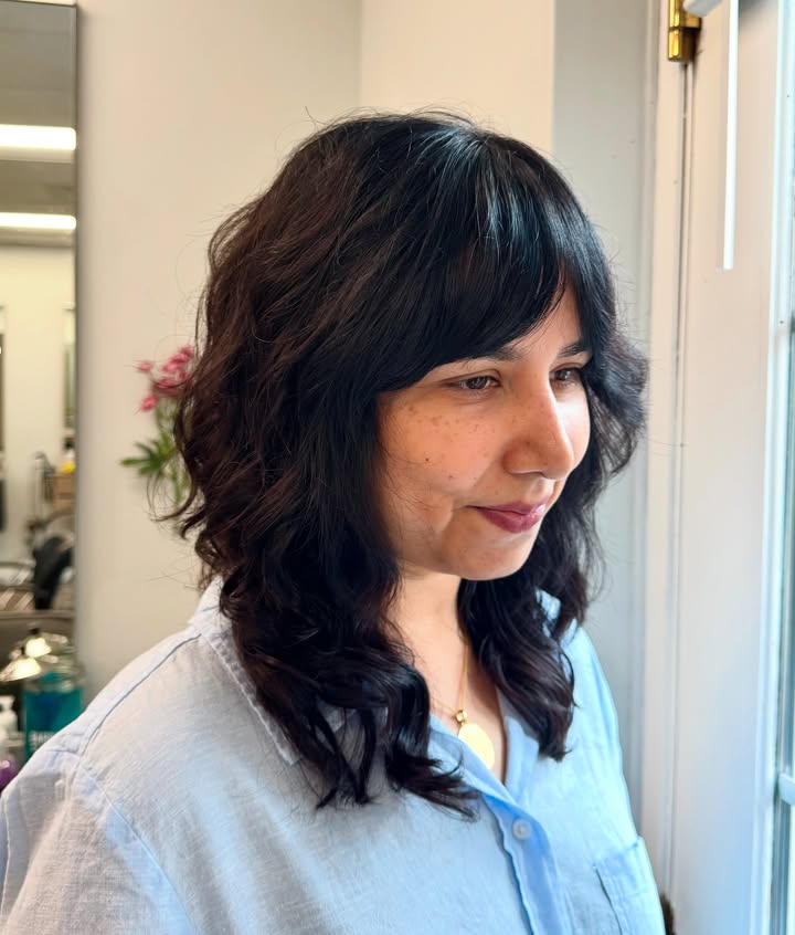 Shoulder length shag haircut with soft layers and feathered bangs in dark brown hair.
