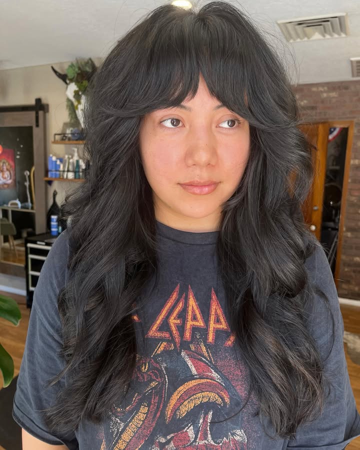 Long layered dark brown hair with soft waves and wispy bangs framing the face.