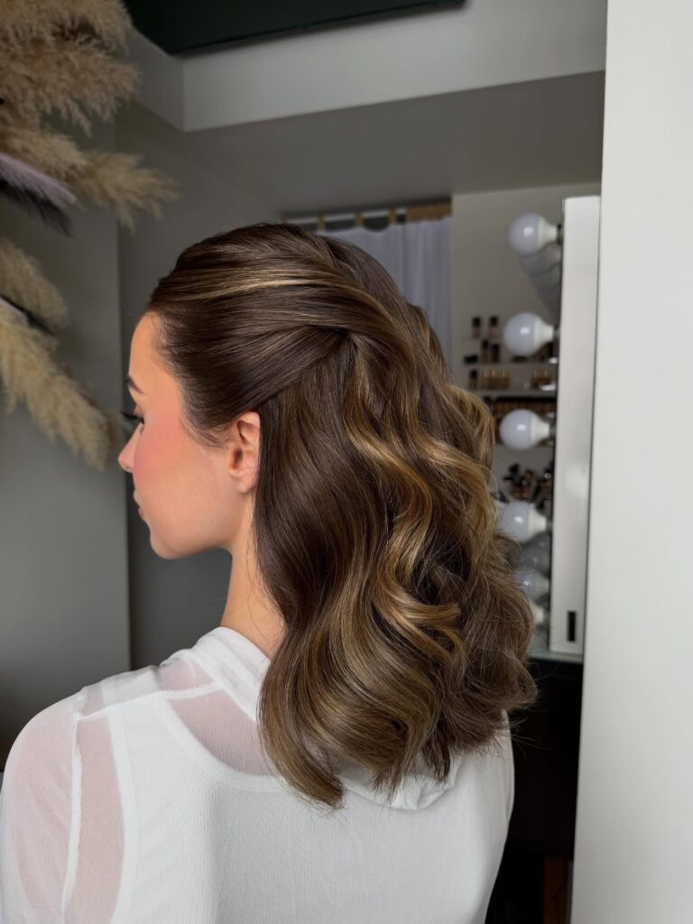 A side view of a woman with medium length wavy brunette hair styled in a half up twisted design.