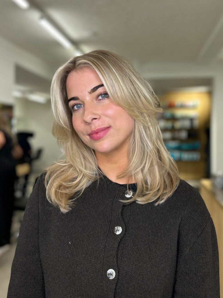 A woman with a shoulder length sandy blonde haircut featuring soft face framing layers and a smooth finish.