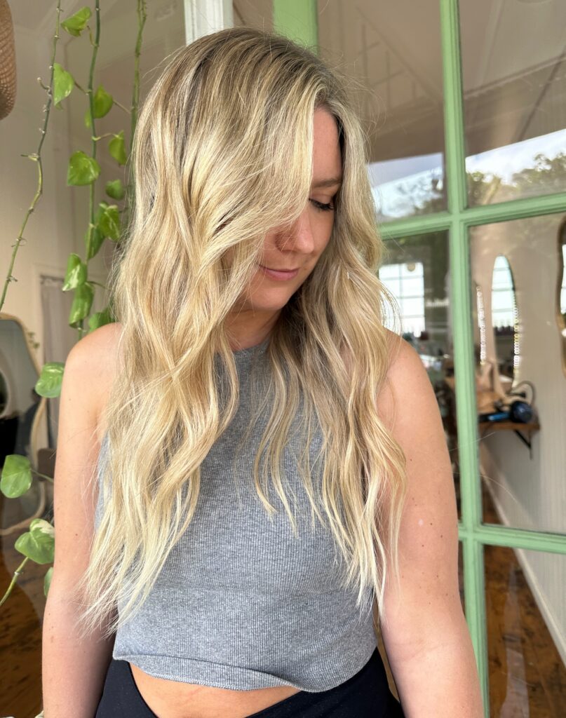 A woman with long honey blonde hair featuring textured beach waves and bright face-framing highlights.