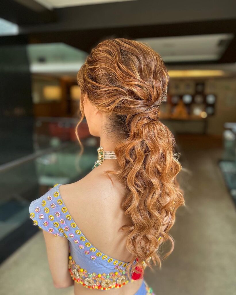 A back view of a woman with vibrant coppery ginger long hair styled into a textured, wavy low ponytail with volume.