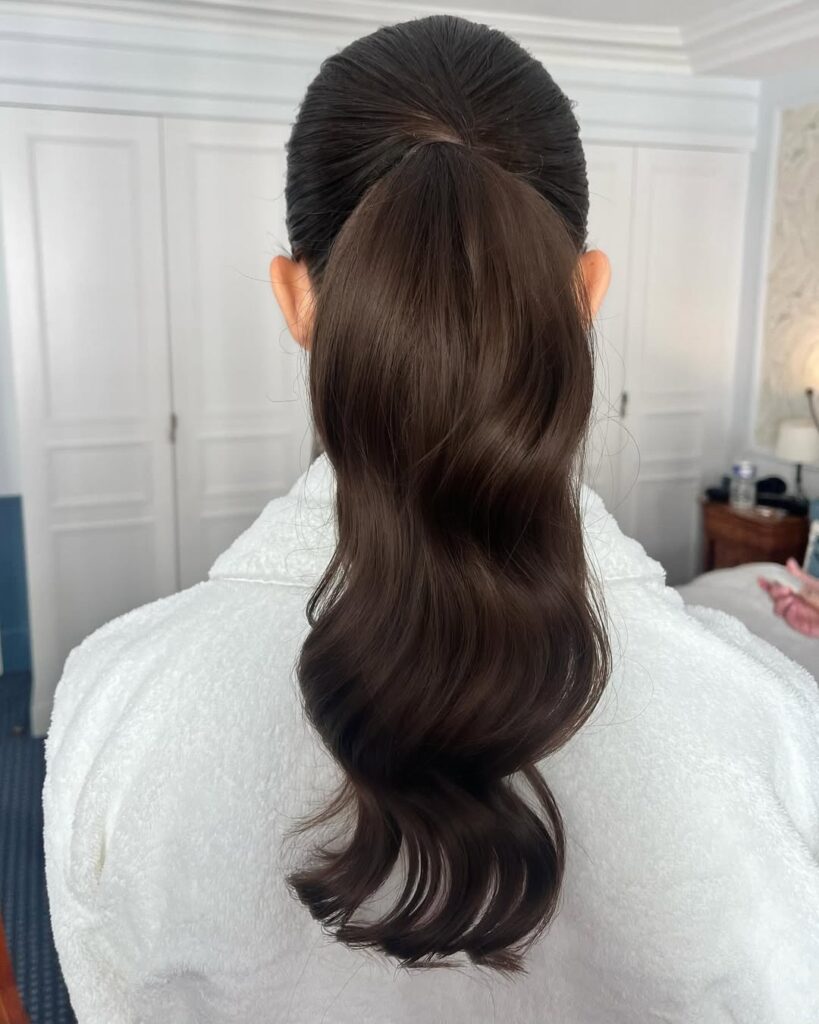 Low ponytail with smooth top and soft waves flowing through the length.