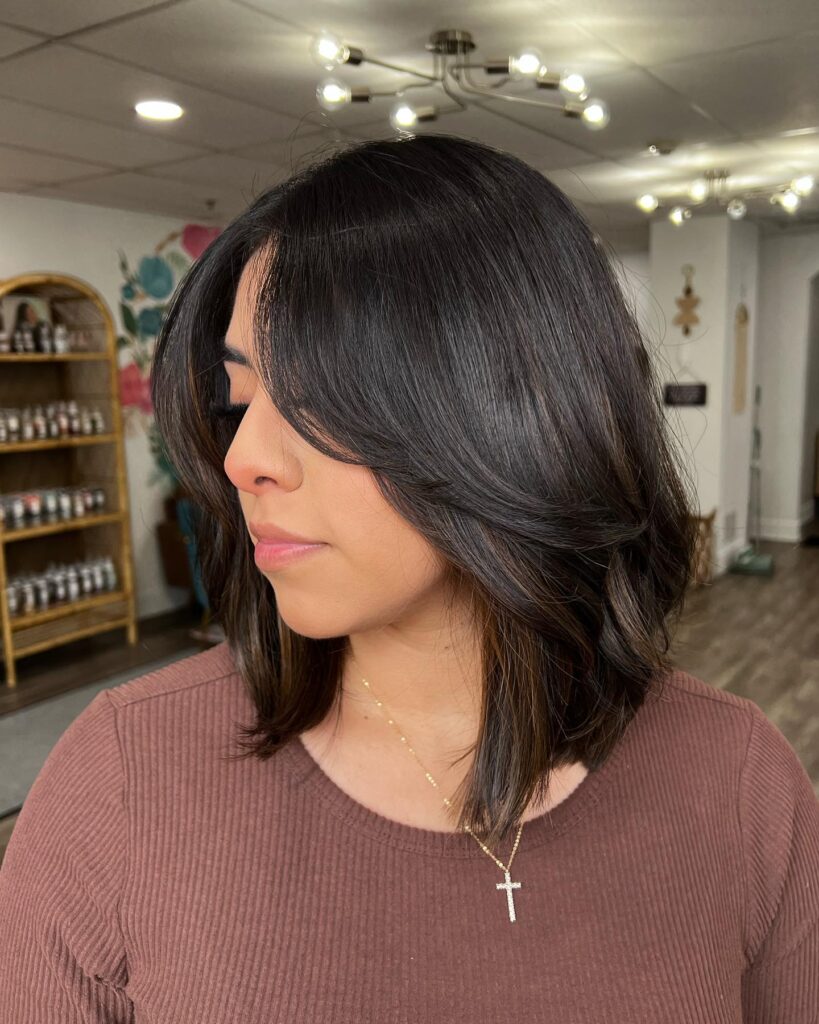 A woman with a short layered brunette lob styled with a soft side part and smooth layers.