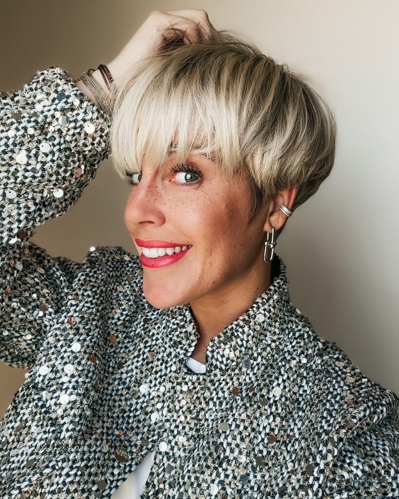 A woman with a feathered blonde pixie haircut with soft layers and volume on top.