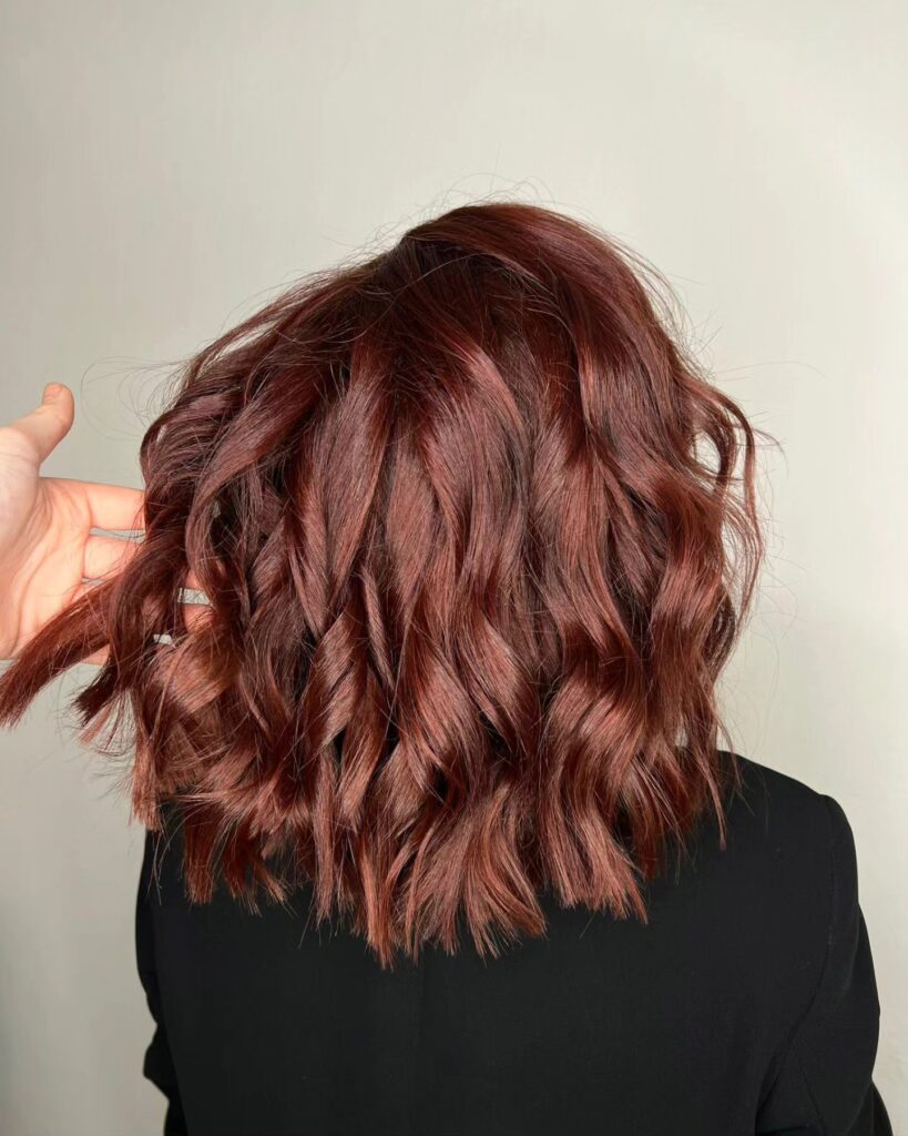 A woman with a short auburn wavy lob featuring soft defined waves and a glossy finish.