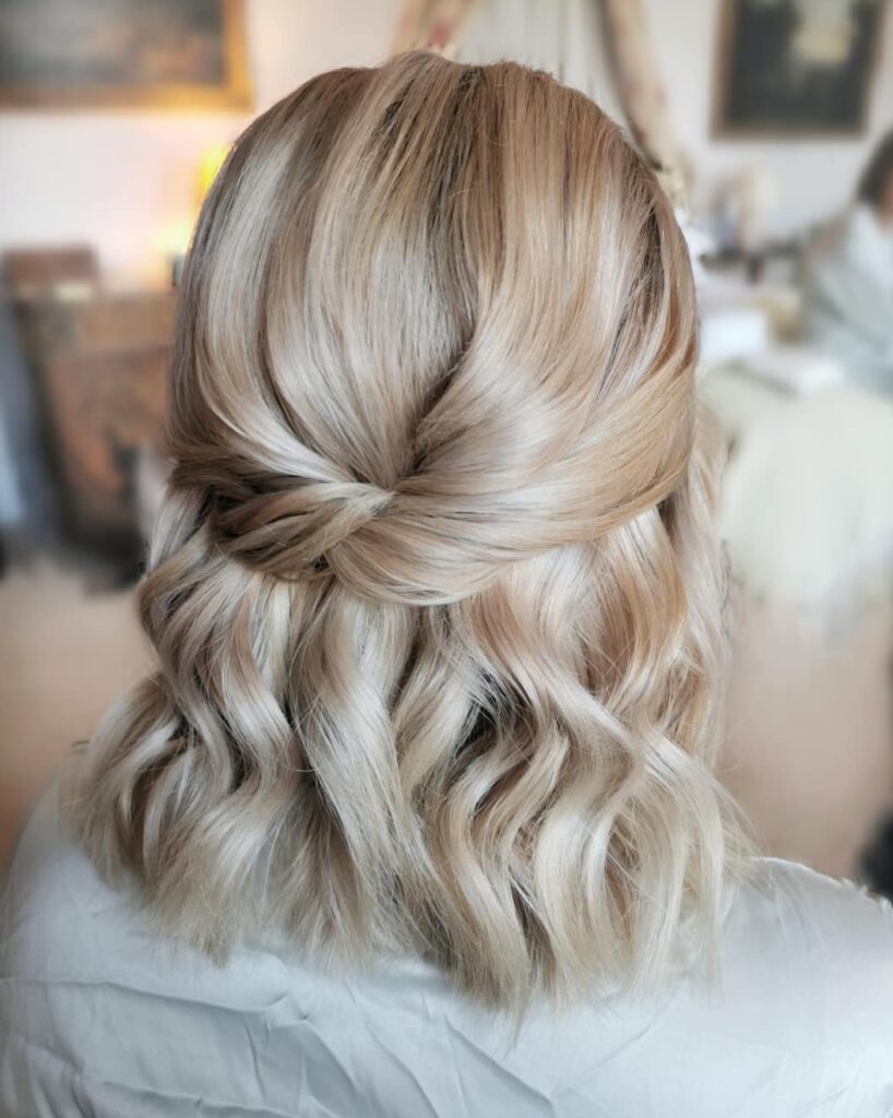 Short blonde hair styled in loose waves with a twisted half up section at the back.
