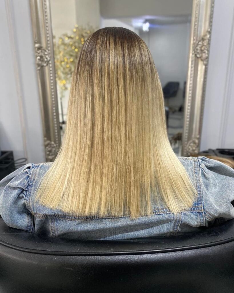 A back view of a person with a straight blunt cut lob featuring bright blonde hair and darker roots.
