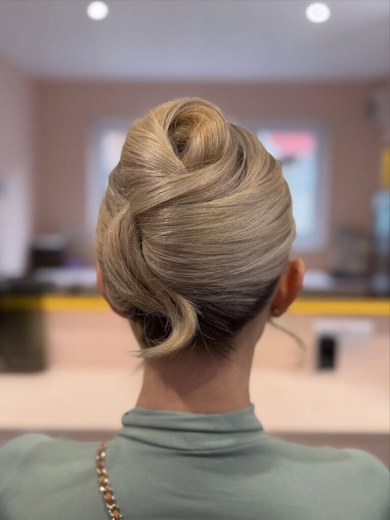 A back view of a woman with long smooth ash blonde hair styled in a structured architectural updo.