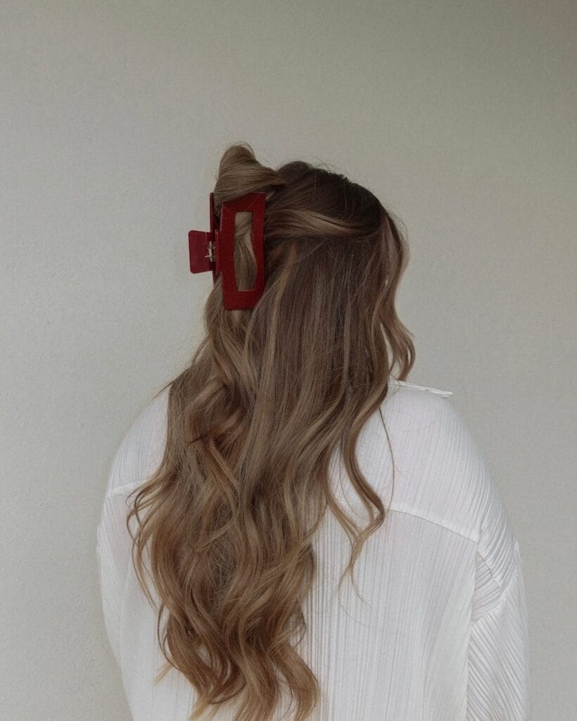 The back view of a woman with long wavy light brown hair in a half up style secured by a large rectangular red claw clip.