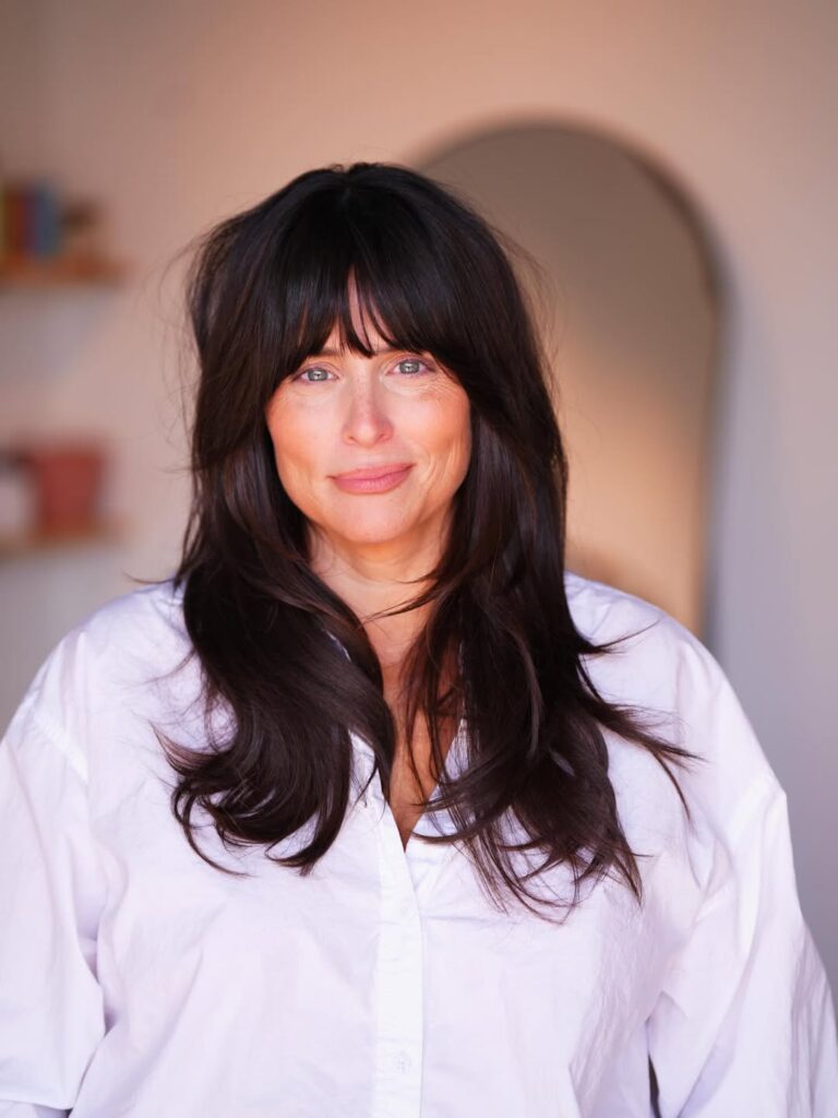 Long dark brunette hair with sleek layers and full curtain bangs framing the face.