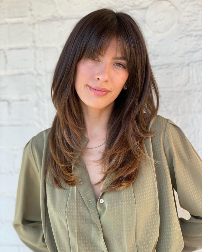 Long sleek brunette hair with soft layers and curtain bangs framing the face.