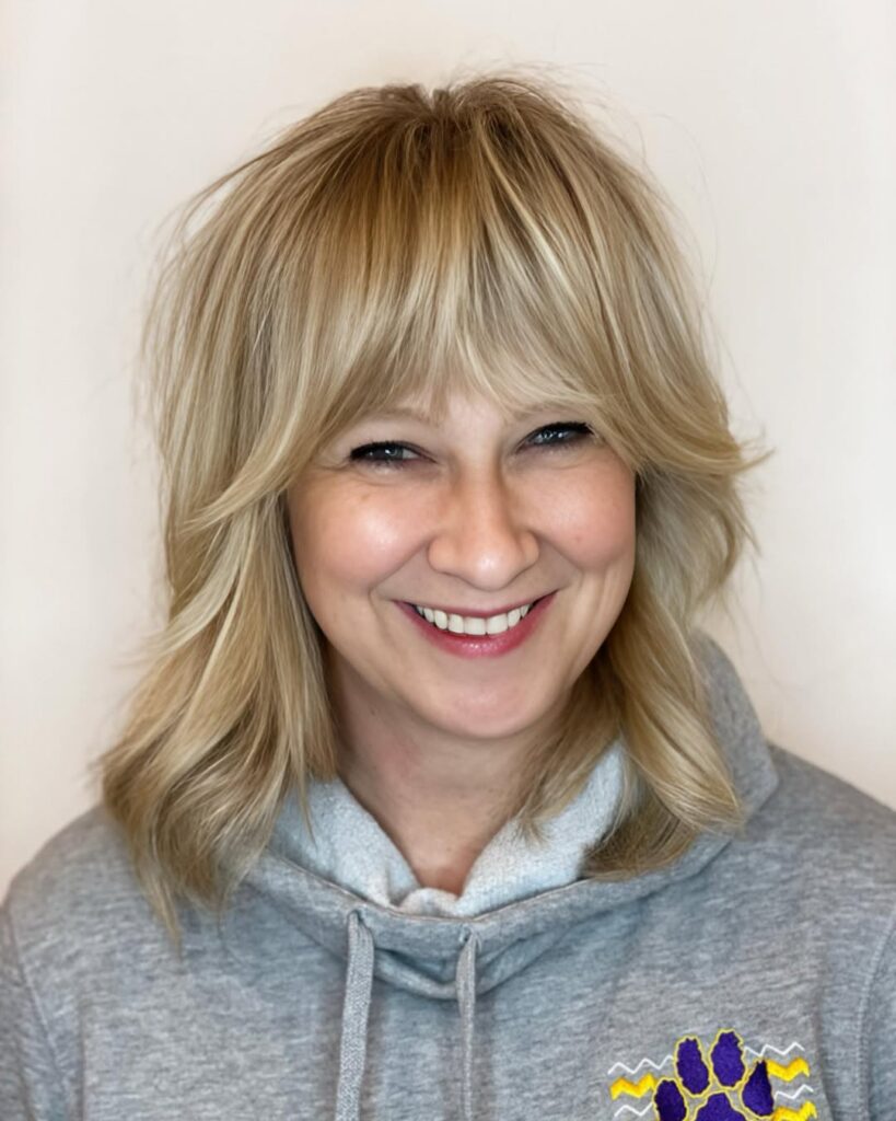 Shaggy layered blonde hair with piecey curtain bangs and a soft textured finish.